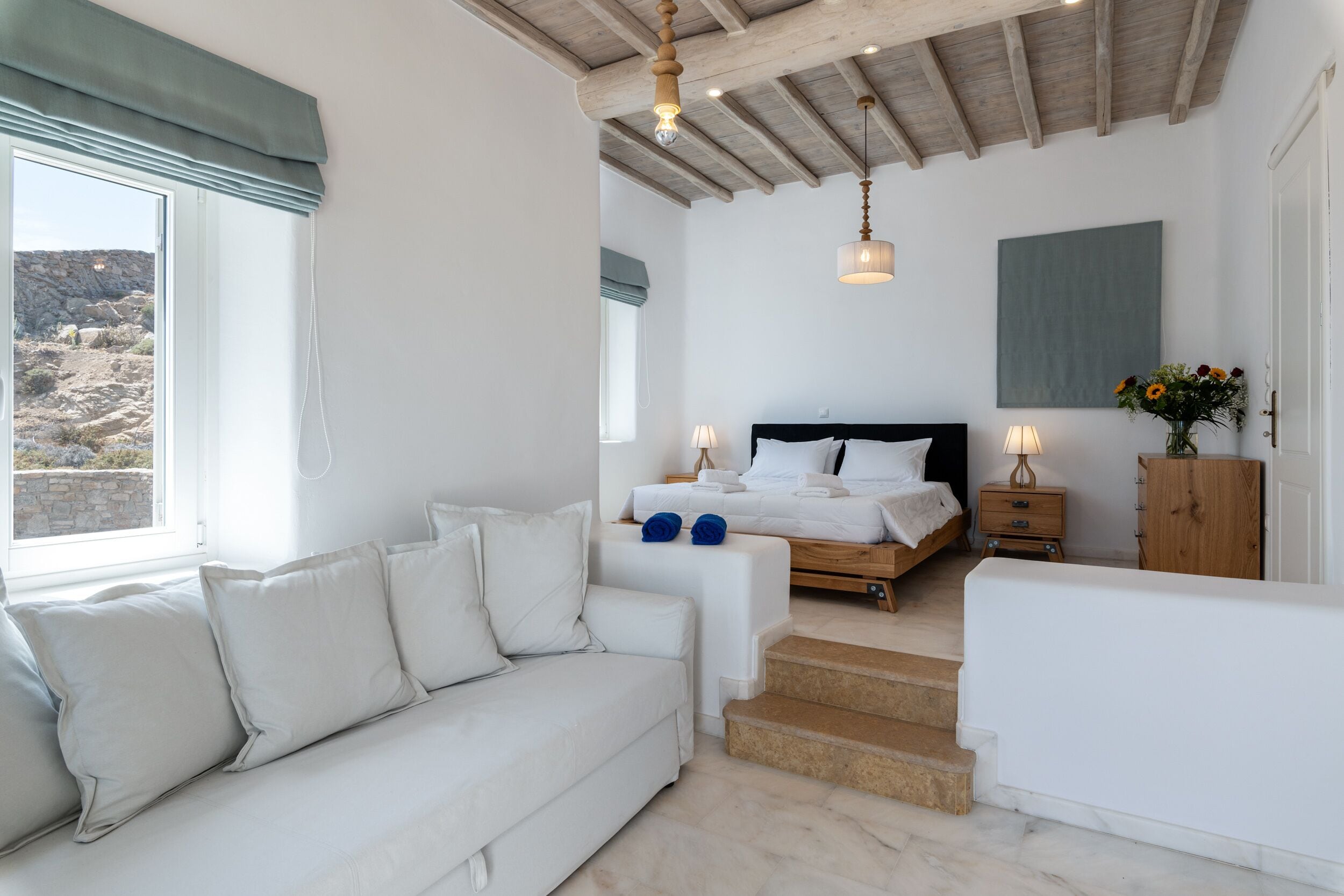 Un dormitorio con cama, sofá, mesita de noche y vistas al exterior.