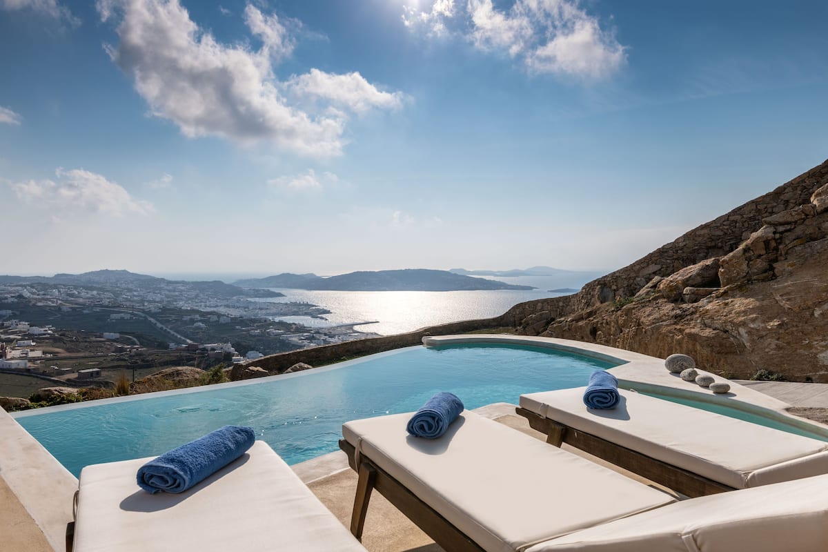 A poolside area with lounge chairs and a view of the sea and landscape.
