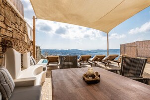 Una terrazza con tavolo in legno, poltrone relax e vista sul mare e sulle montagne.