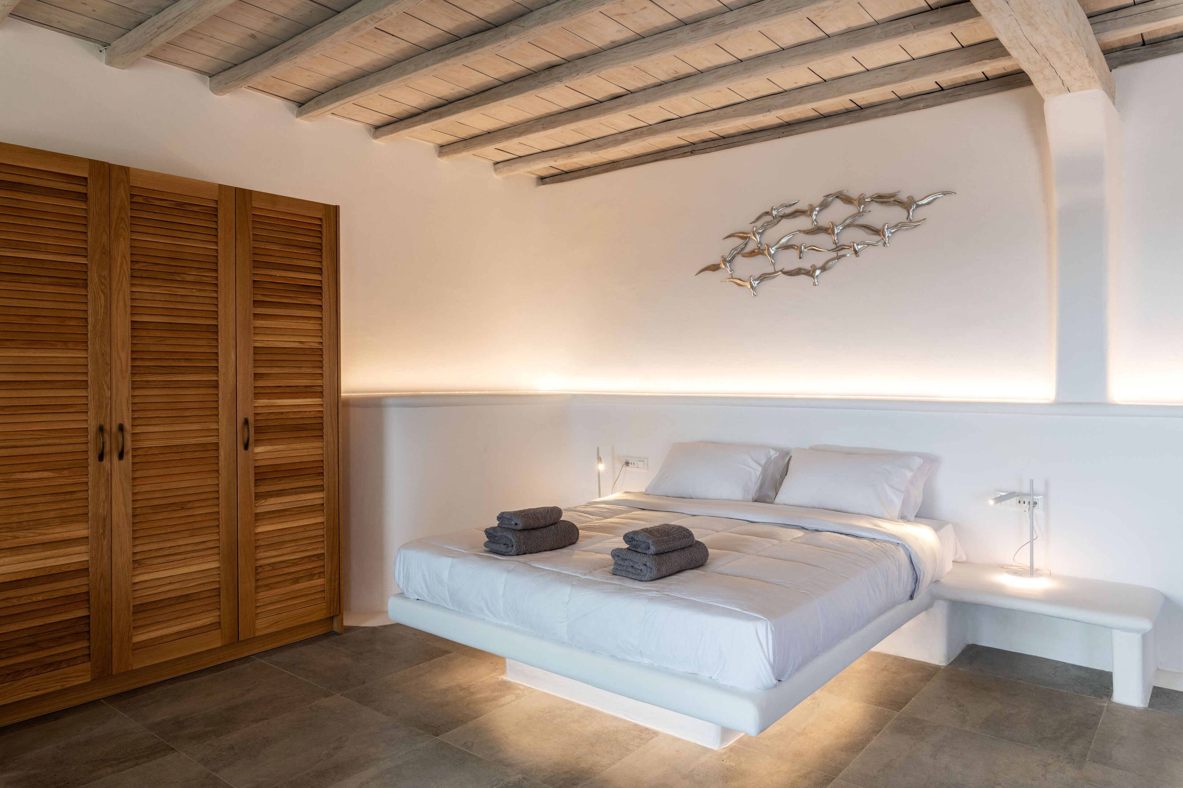 A bedroom with a bed, bedside tables, a wooden wardrobe, and a ceiling with exposed beams.