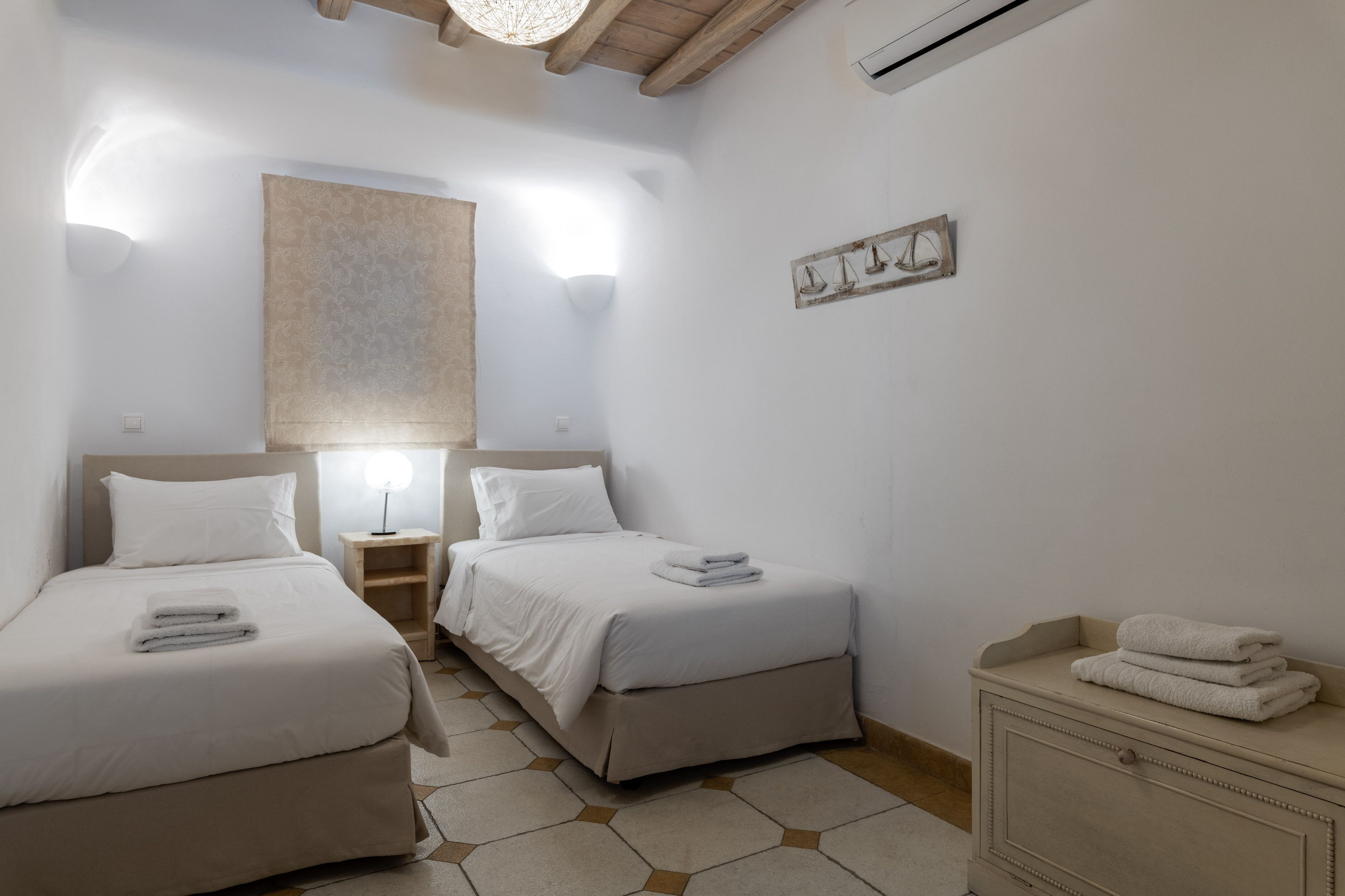 Un dormitorio con dos camas, una mesita de noche, un aparador y un estante en la pared con objetos decorativos.