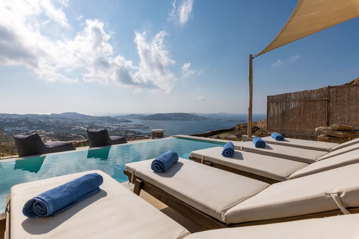 A poolside area with lounge chairs and a view of the sea and distant landscape.