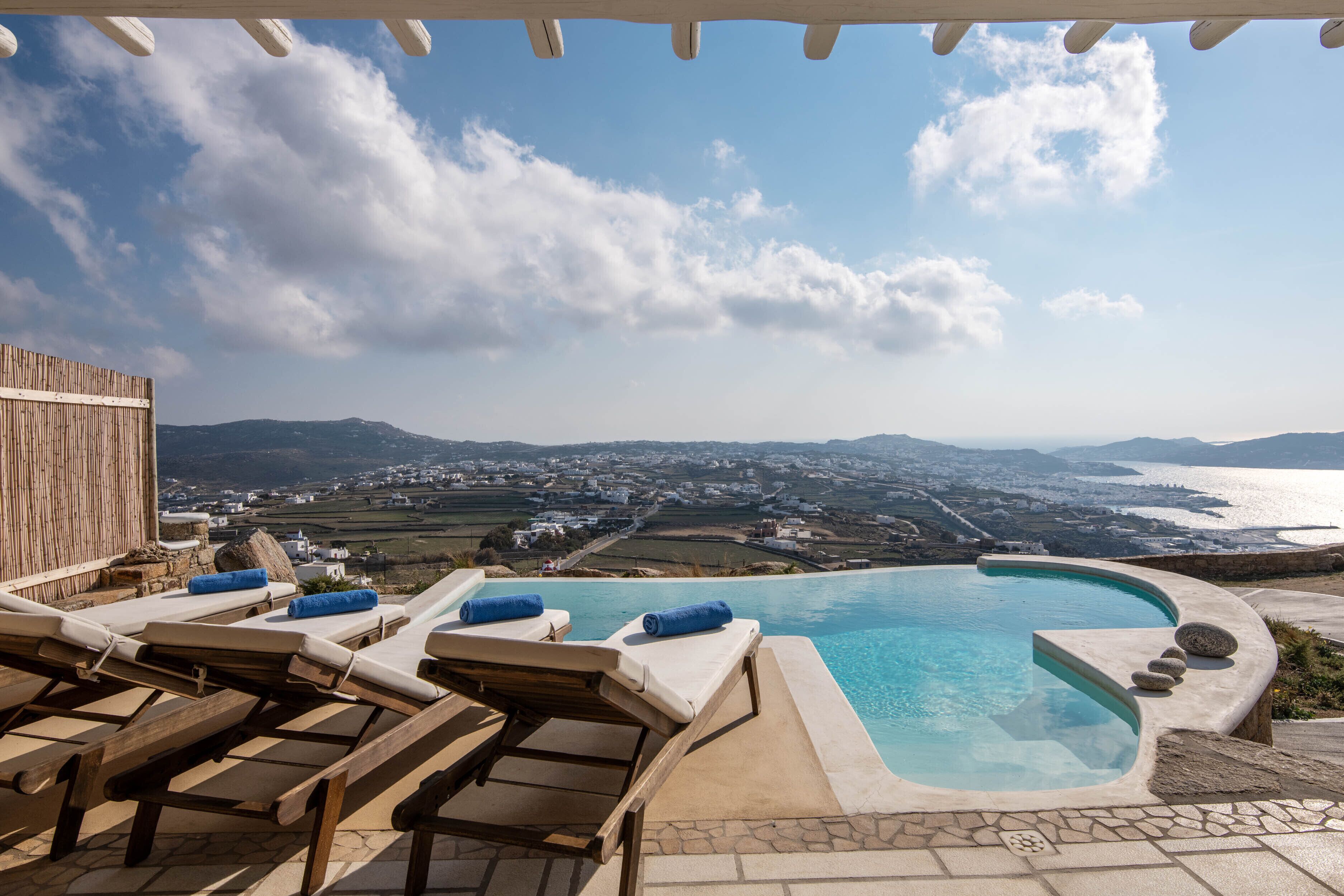 A pool area with lounge chairs and a view of the sea and distant landscape.