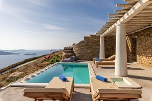 Área de piscina com espreguiçadeiras e um pérgola com vista panorâmica.