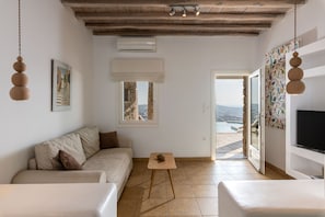 Un salón amplio con un sofá color beige, una mesita de madera y un televisor sobre un mueble blanco. Un ventanal ofrece vistas al exterior.