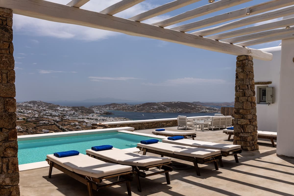 A poolside area with lounge chairs and a view of a coastal town.