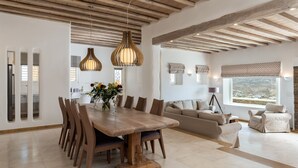 A spacious living area with a wooden dining table, multiple chairs, a sofa, and a window with a view. - Mykonos Divino (Mykonos)