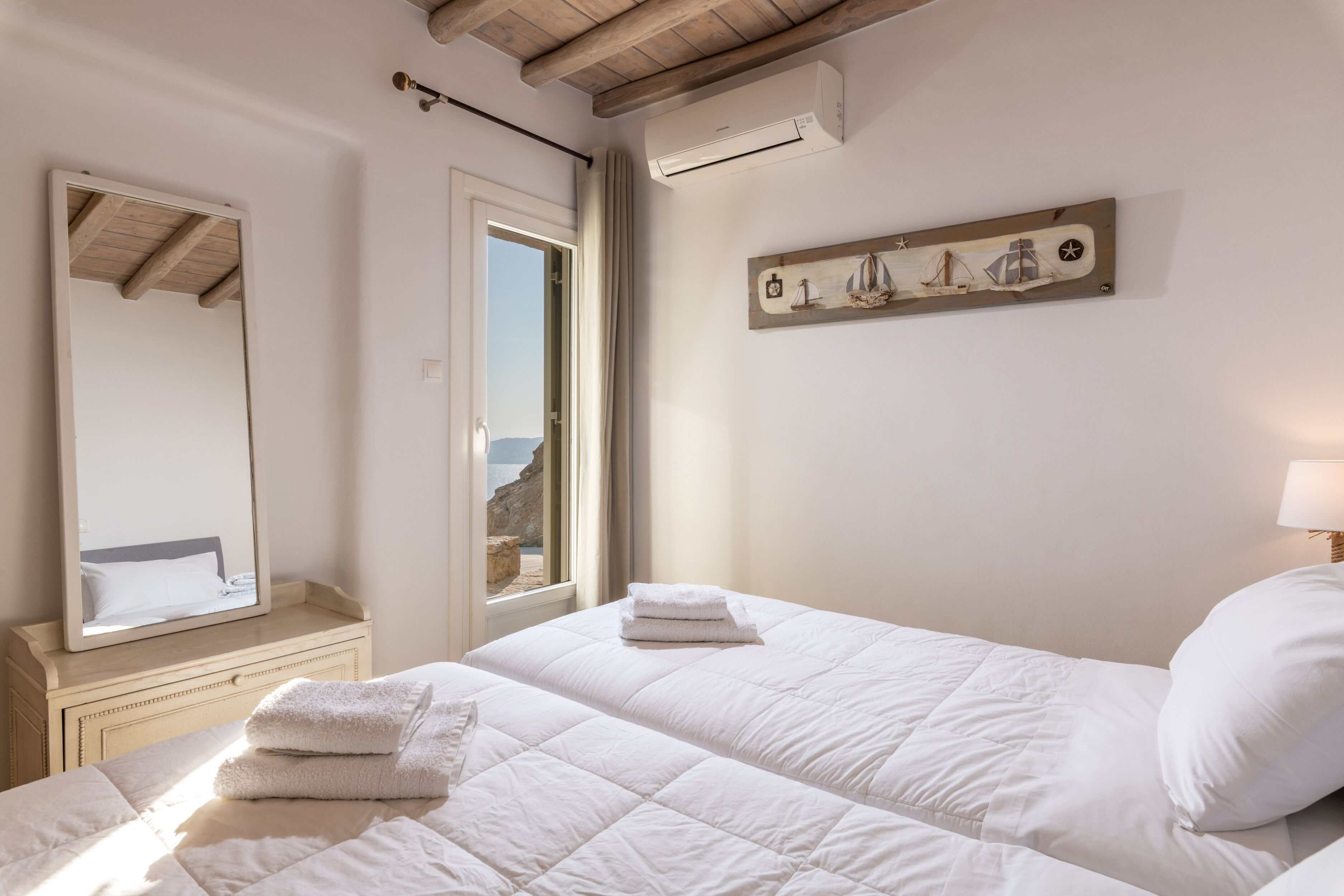 A bedroom with a bed, a mirror, a window, and a wall-mounted artwork.