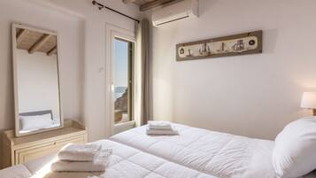 A bedroom with a bed, a mirror, a window, and a wall-mounted artwork.