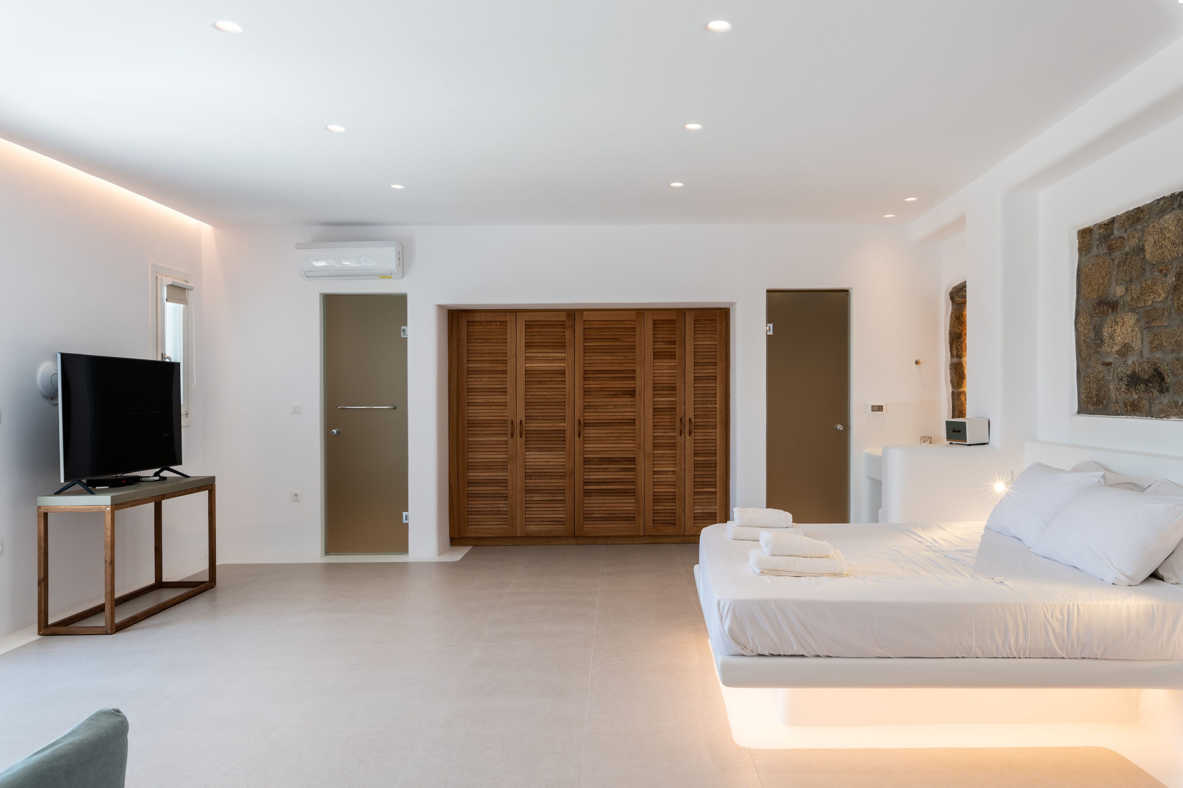 A modern bedroom with a bed, a TV on a stand, a wardrobe, and a painting on the wall.