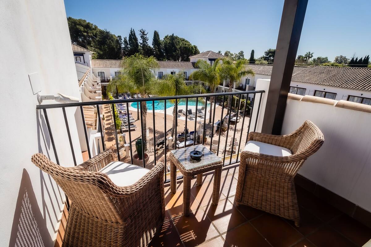 A balcony with wicker furniture, a pool, and a view of a resort area.