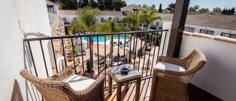 A balcony with wicker furniture, a pool, and a view of a resort area.