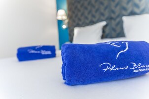 Een netjes opgemaakt bed met een blauwe handdoek en een blauw kussen met de tekst 'Paloma Blanca boutique.com'.