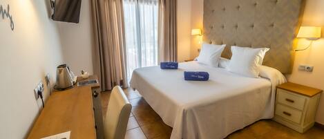 A hotel room with a bed, bedside lamps, a desk with a telephone, and a television on the wall.