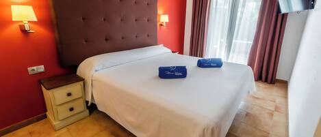 A hotel room with a large bed, two bedside tables, a flat-screen TV, and a window with curtains.