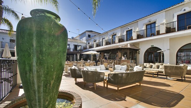 Un patio al aire libre con mobiliario de mimbre, un jarrón verde grande y piso de baldosas.