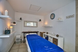Een kamer met een bed, een bureau, een spiegel, planken met kaarsen, een klok en een kleine tafel met een vaas.
