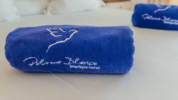 Een keurig opgemaakt bed met witte lakens en een blauwe handdoek met borduurwerk.