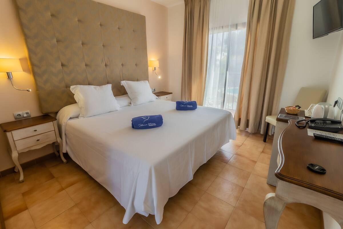 A hotel room with a large bed, a wooden nightstand, a desk with a telephone and a basket, and a television on the wall.
