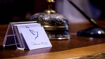 A brochure stand with a white card displaying a logo and text, a decorative glass object, and a pen on a wooden surface.