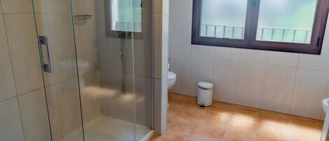 A bathroom with a glass-enclosed shower, a window with a view, and a tiled floor.