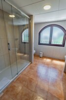Een badkamer met een douchecabine van glas, een raam met uitzicht en een betegelde vloer.