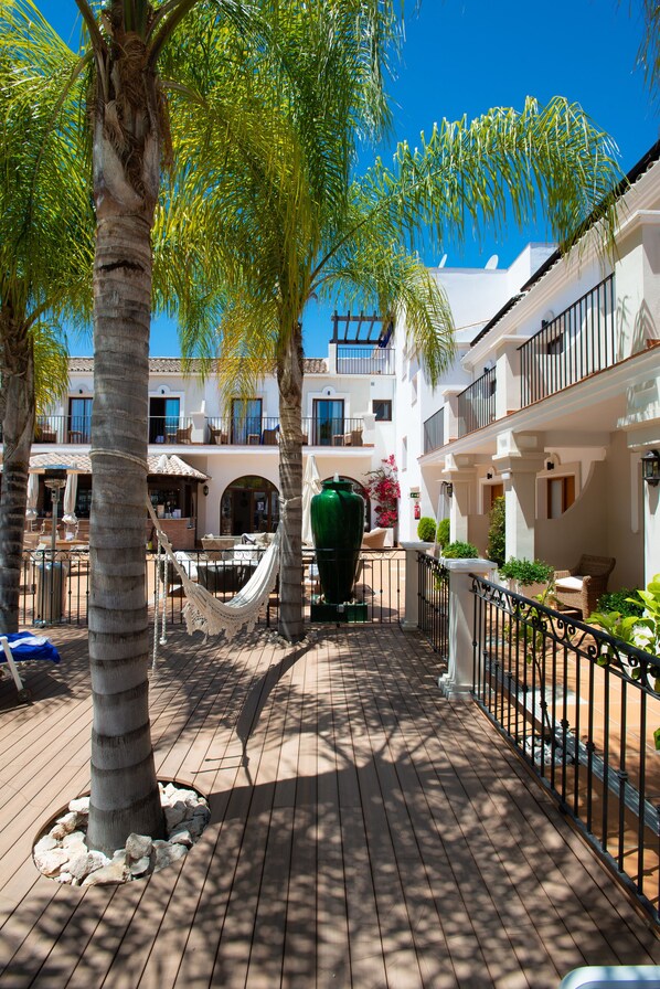 Un patio con palmeras, mobiliario exterior y un gran jarrón verde.