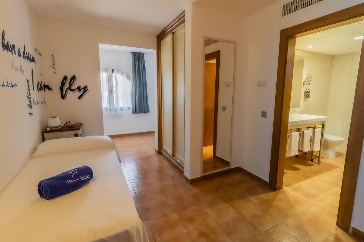 A hotel room with a bed, a bathroom visible through an open door, and motivational wall art.