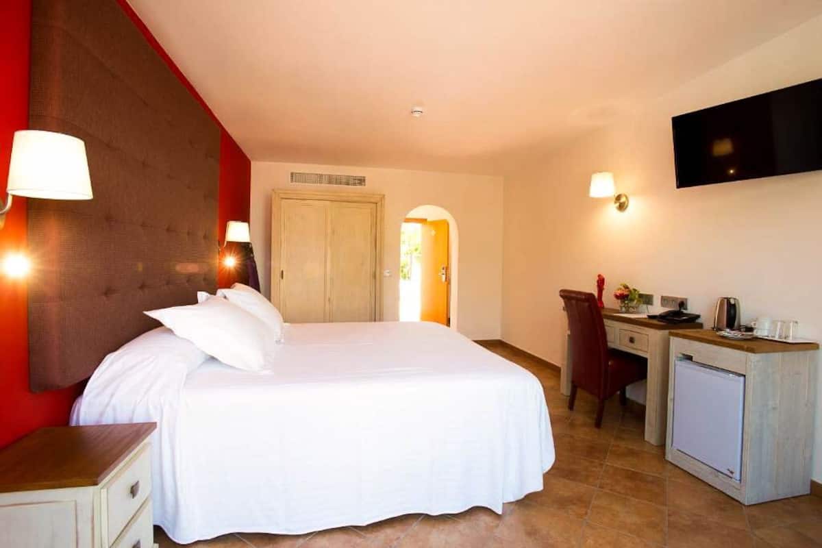 A hotel room with a bed, a desk, a chair, a TV, and a small kitchenette.