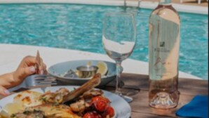 Mesa de comedor junto a una piscina, con un plato de comida, una botella de vino y una copa.