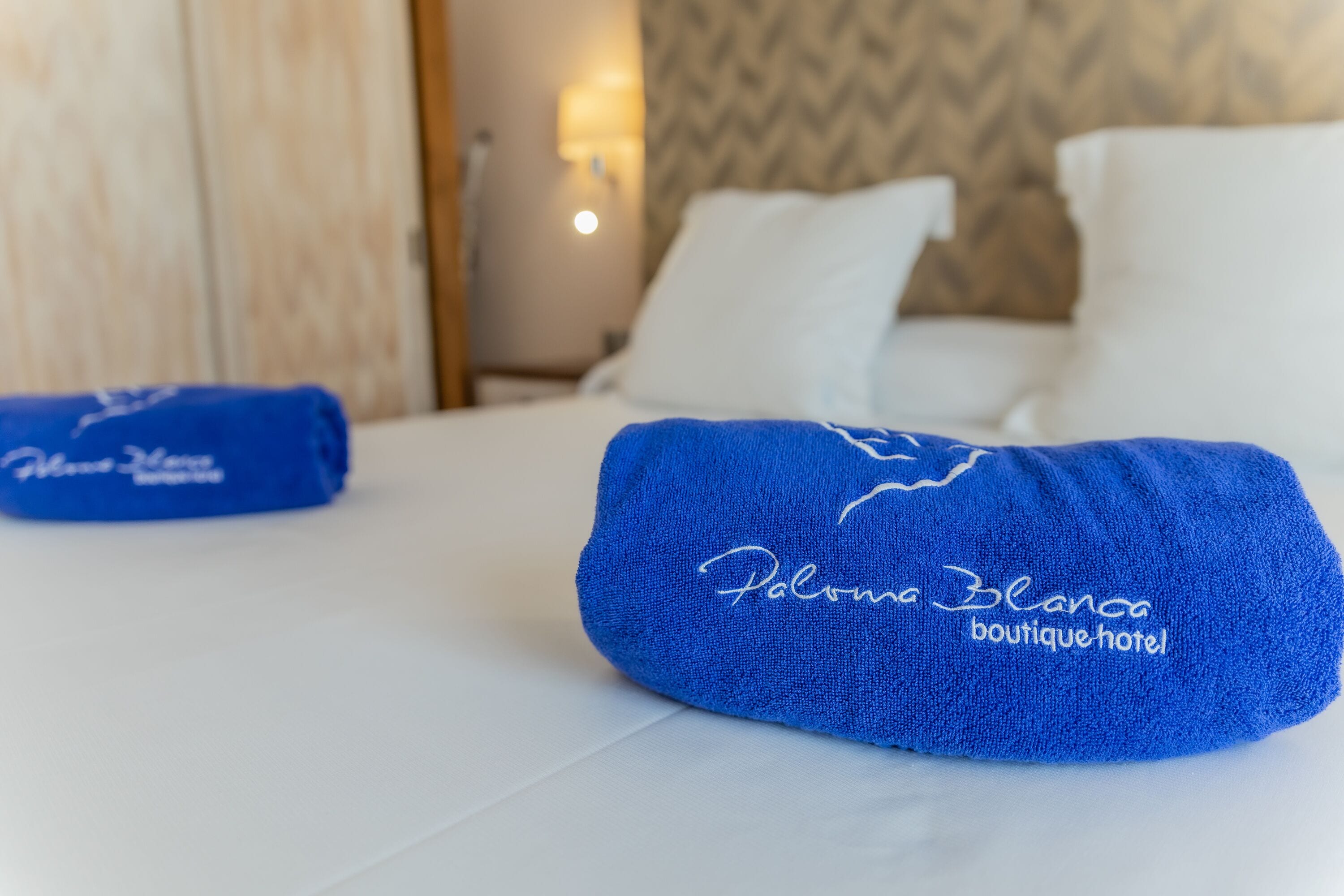 Una cama bien hecha con sábanas blancas y una toalla azul con texto bordado.