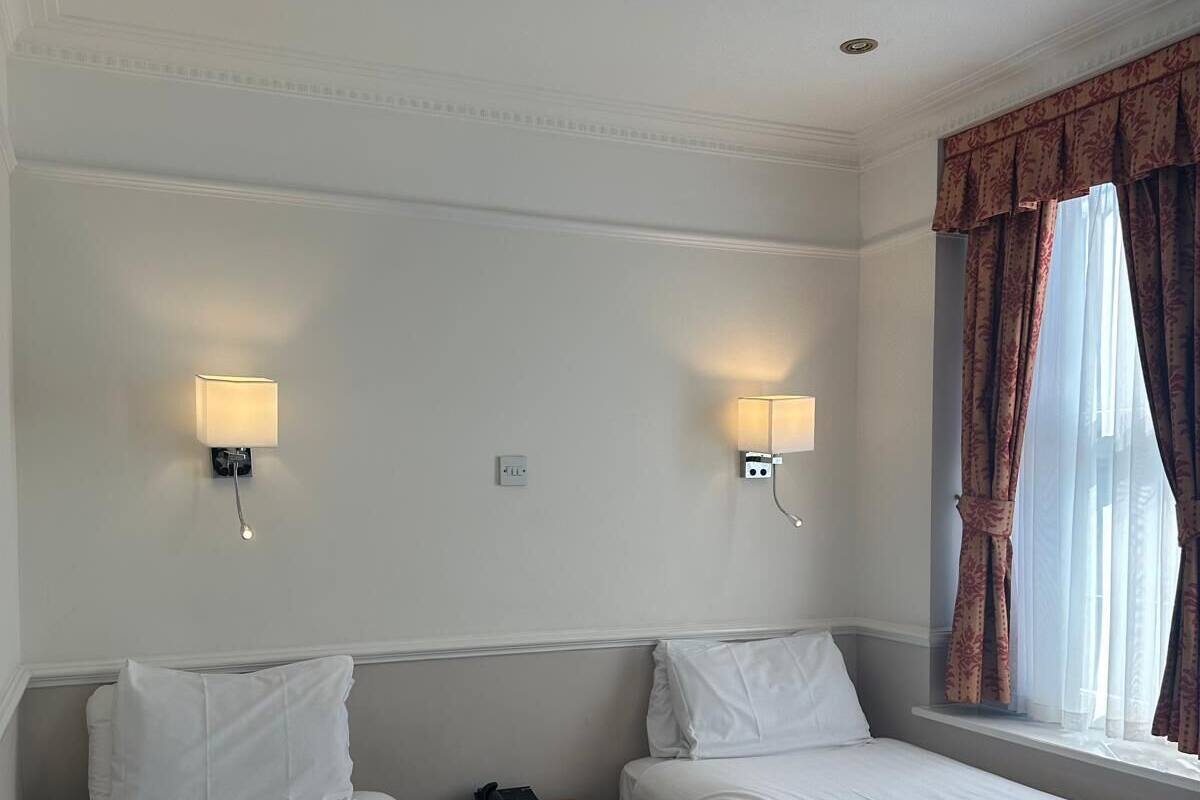 A hotel room with two single beds, a bedside table with a phone, and two wall-mounted lamps.