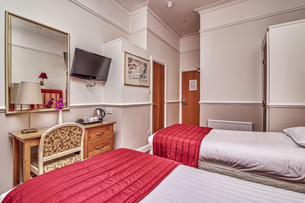 A hotel room with two beds, a desk, a chair, a television, and a mirror.