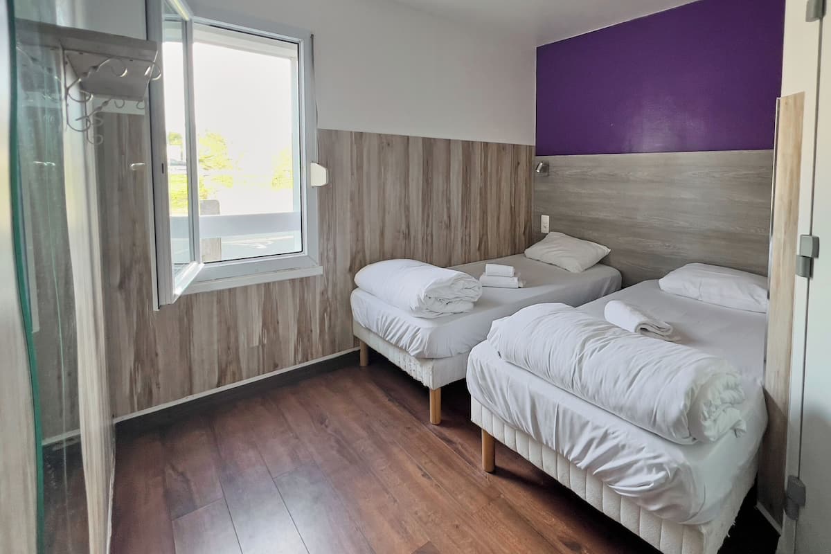 Quarto com duas camas, piso de madeira, janela e uma parede com detalhes em roxo.