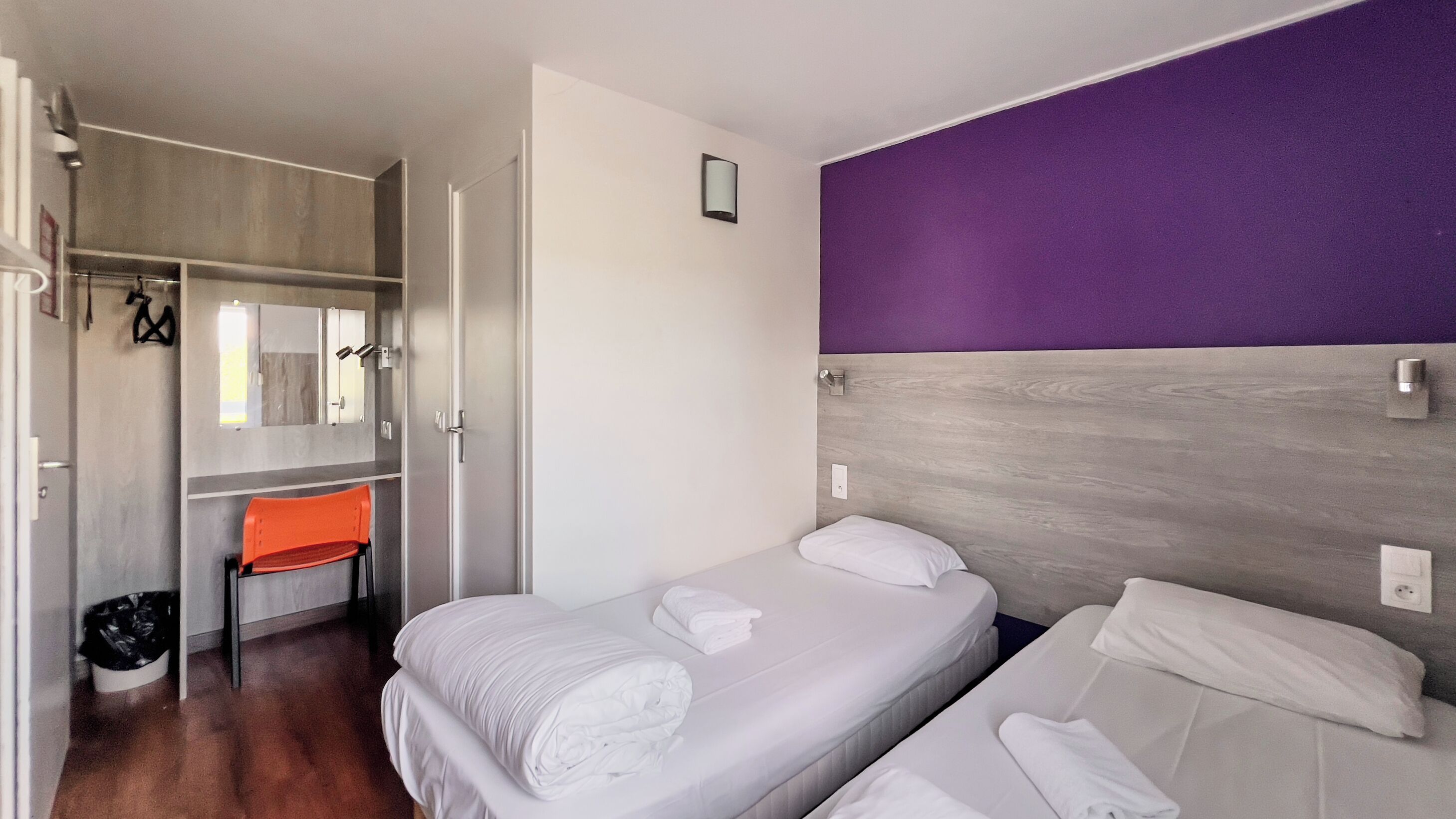 A hotel room with two beds, a bathroom, and a seating area with a chair and a small table.
