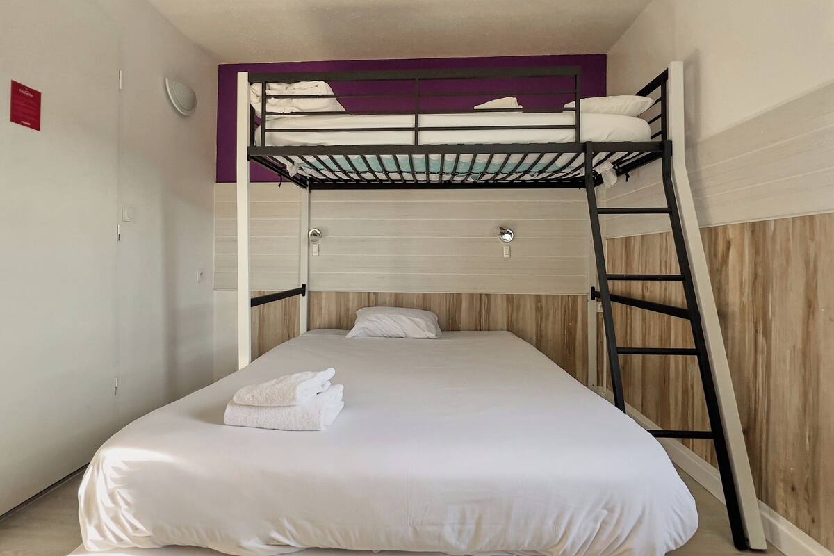 Quarto com beliche, cabeceira de madeira, colchão branco e toalha branca na parte de baixo.