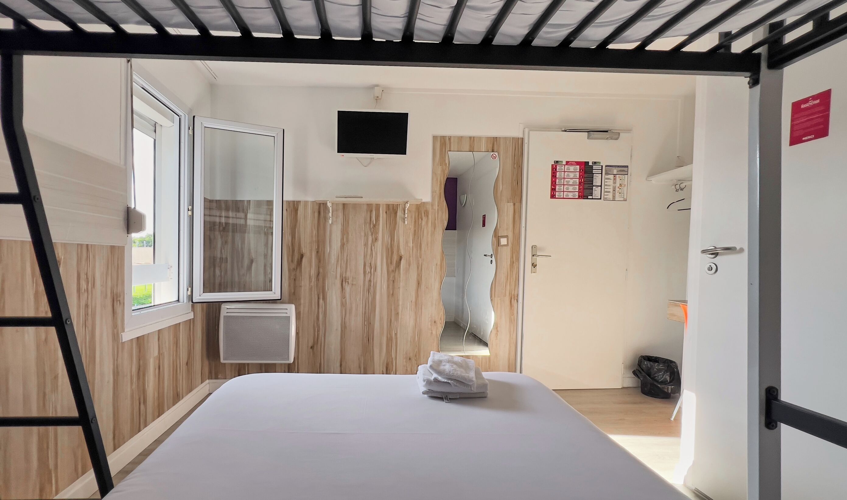 A room with a bed, a window, a TV, and a door with a sign.