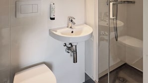 A modern bathroom with a toilet, sink, and glass-enclosed shower. - Fasthotel La Roche sur Yon Un FH CONFORT (La Roche-sur-Yon)