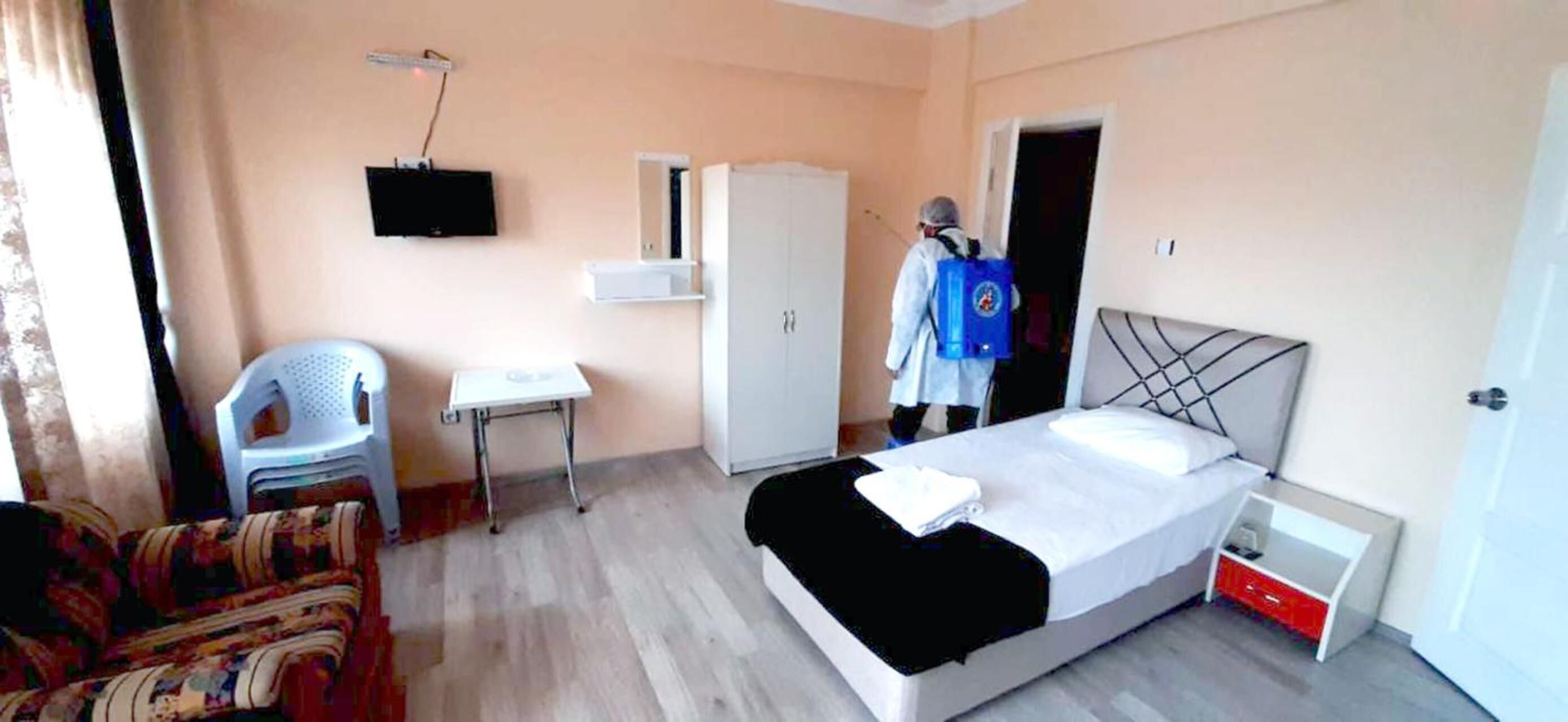 A hotel room with a bed, a desk, a chair, a wardrobe, and a television on the wall.