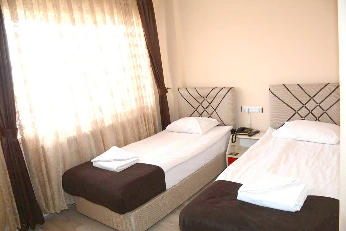 A hotel room with two single beds, a nightstand with a phone, and a window with curtains.