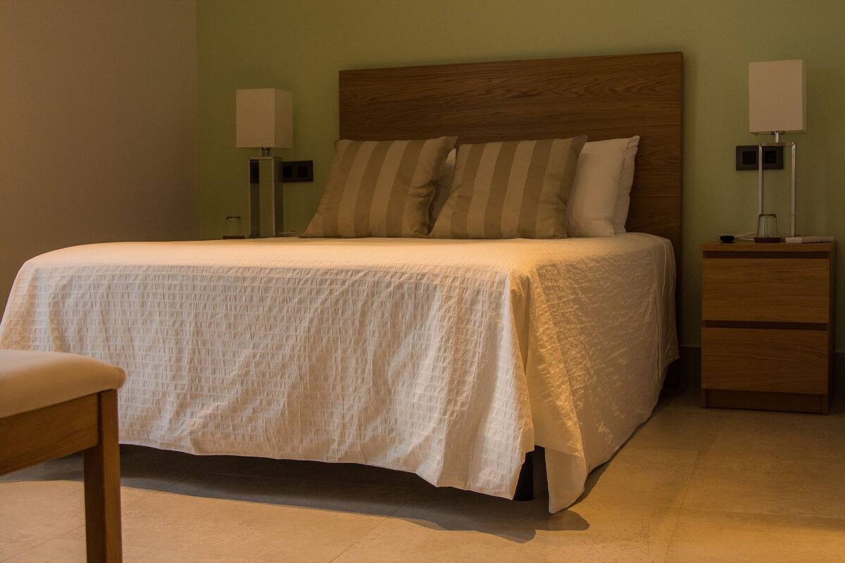 A neatly made bed with a wooden headboard, two bedside lamps, a wooden nightstand, and a chair.