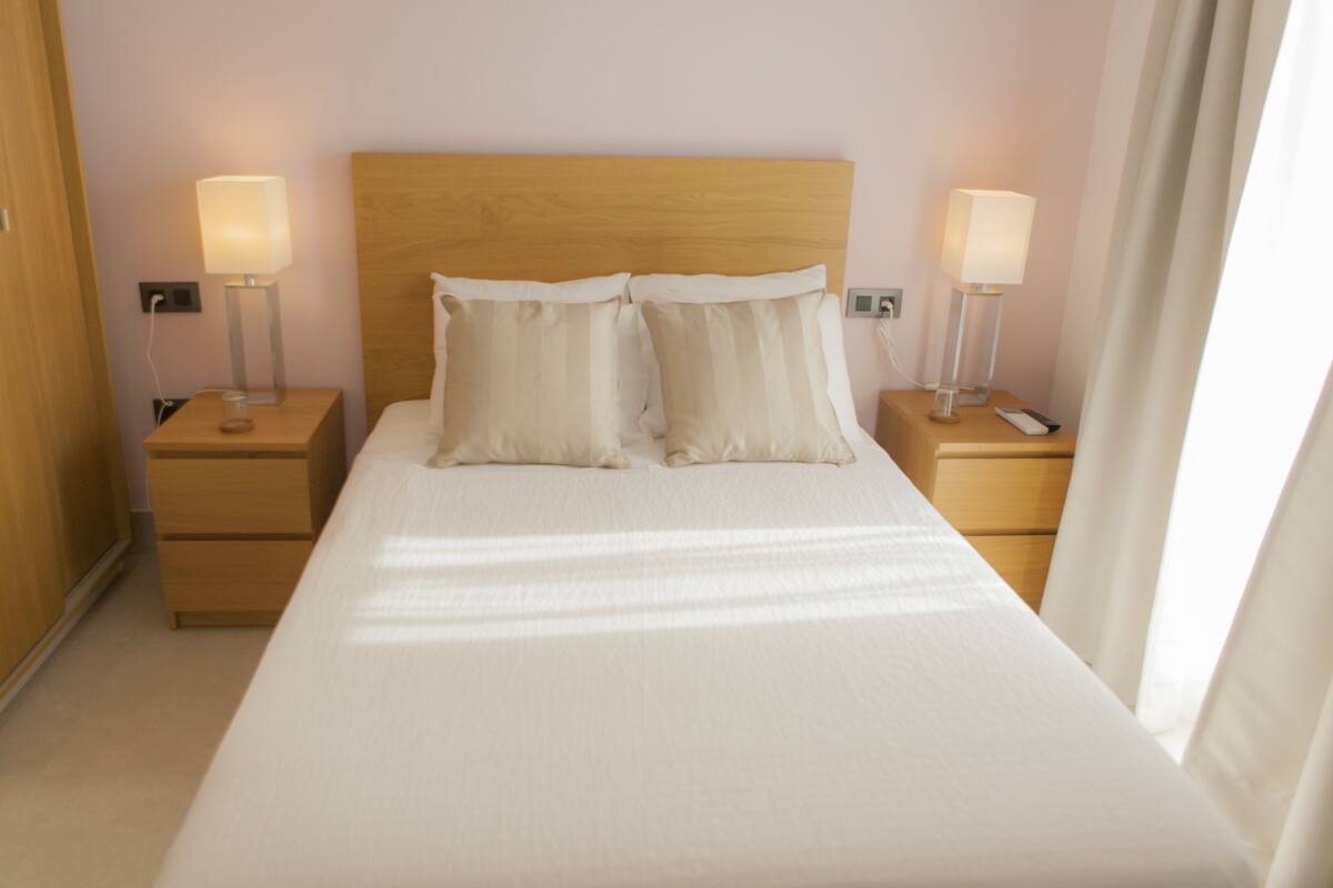 A neatly made bed with white linens and two pillows, flanked by wooden nightstands with lamps.