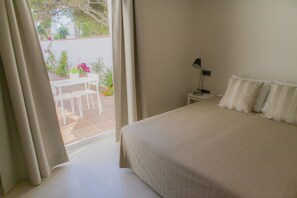 A bedroom with a large bed, a bedside table with a lamp, and a view of an outdoor patio with a table and chairs. - Hotel Novomar (Chiclana de la Frontera)