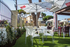 An outdoor patio with white plastic chairs and tables, surrounded by a brick wall and a metal fence. - Hotel Novomar (Chiclana de la Frontera)