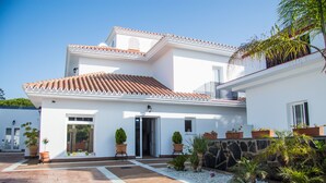 A modern two-story house with a tiled roof, a stone wall, and a paved driveway.