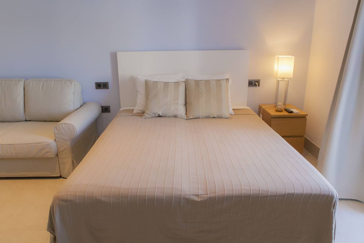 A hotel room with a bed, a nightstand with a lamp, and a sofa.