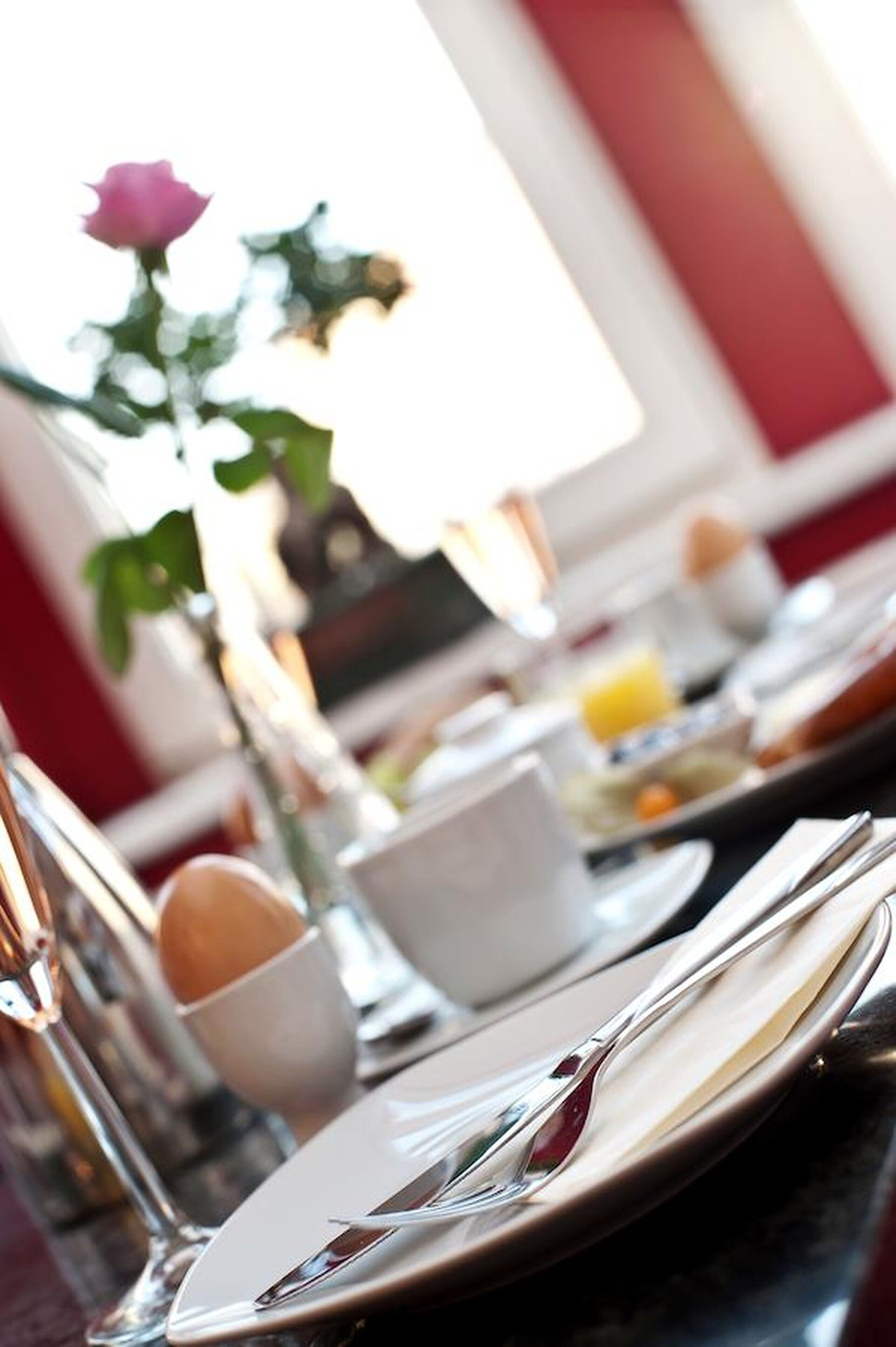 A dining table set with plates, cutlery, and a vase with a single rose.