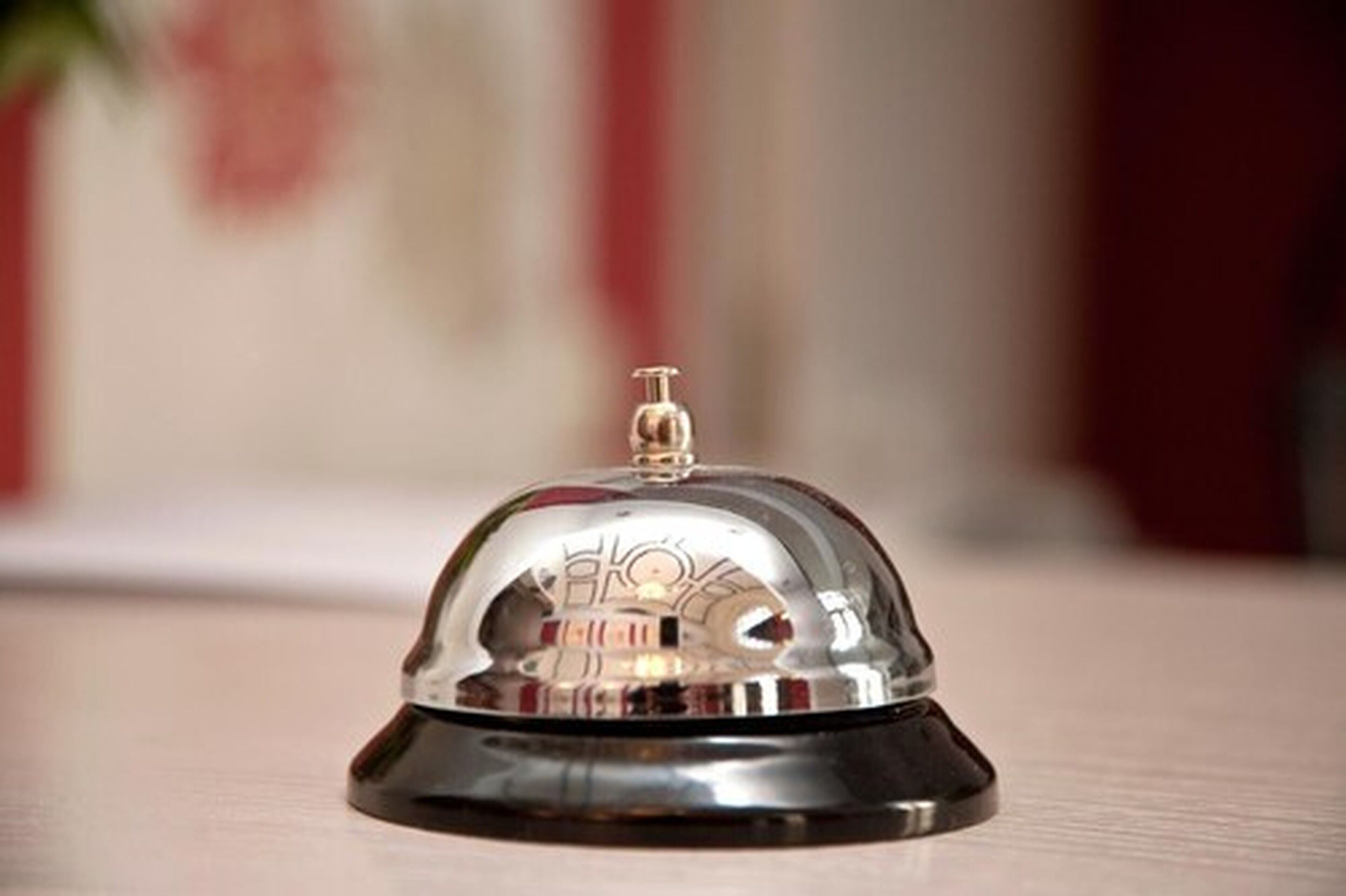A metallic, reflective service bell with a black base, placed on a wooden surface.