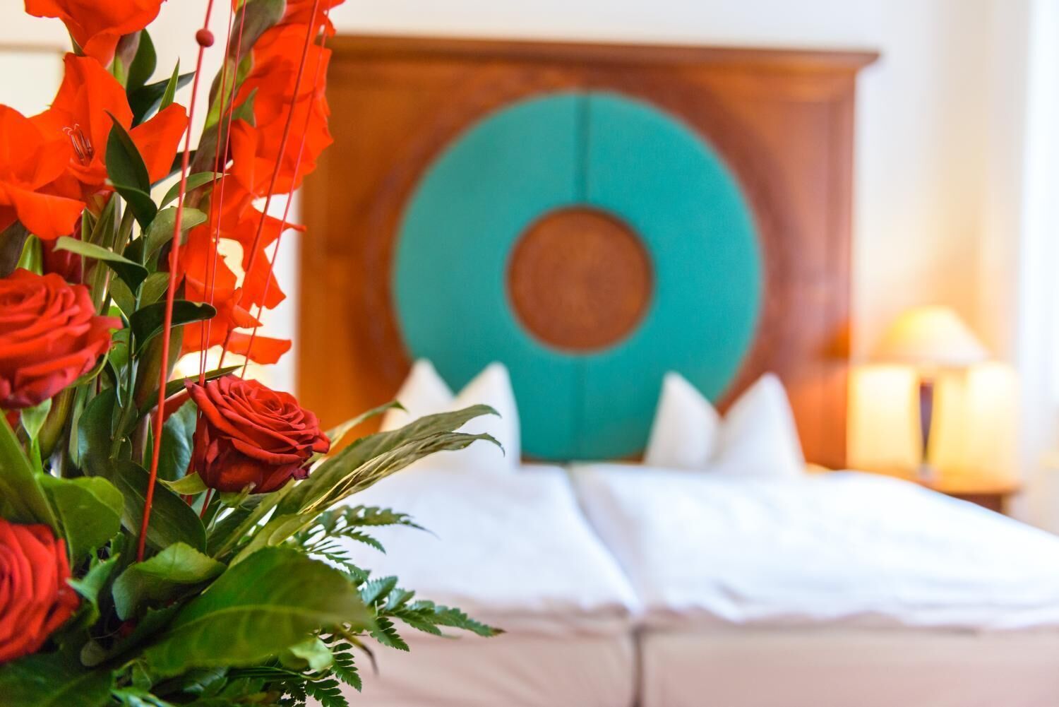 A hotel room with a bed, a wooden headboard, and a large circular teal accent on the wall.