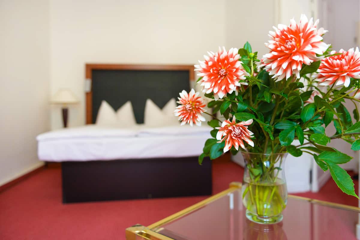 A bed with white bedding and a black headboard, a bedside table with a lamp, and a vase with flowers on a glass table.